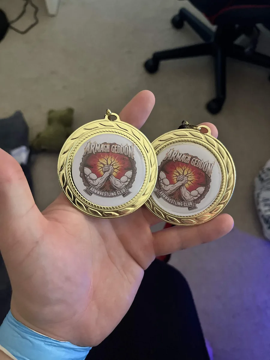 Two gold armwrestling medals held in a hand